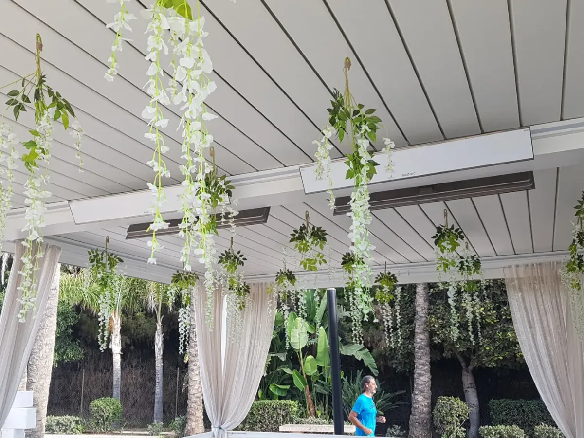 Gibus bioclimatic pergola with white Bromic Platinum Electric heaters, hanging plants and white curtains, on a beachfront property in Marbella