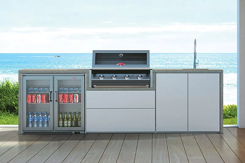 BeefEater built-in barbecue in a white outdoor kitchen with a drinks fridge, on a timber deck overlooking the beach and the sea