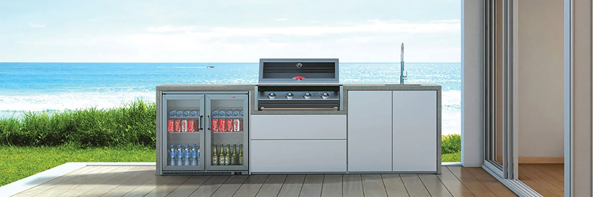 BeefEater built-in barbecue in a white outdoor kitchen with a drinks fridge, on a timber deck overlooking the beach and the sea