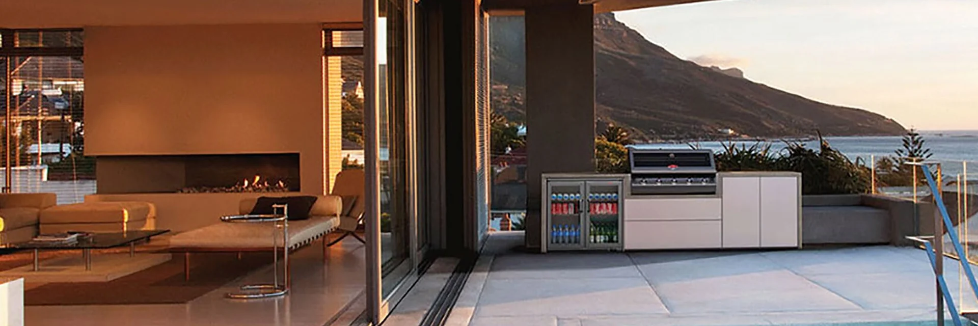BeefEater built-in barbecue and outdoor kitchen cabinets on the terrace of a modern villa at dusk, beside a pool with the sea and a headland beyond