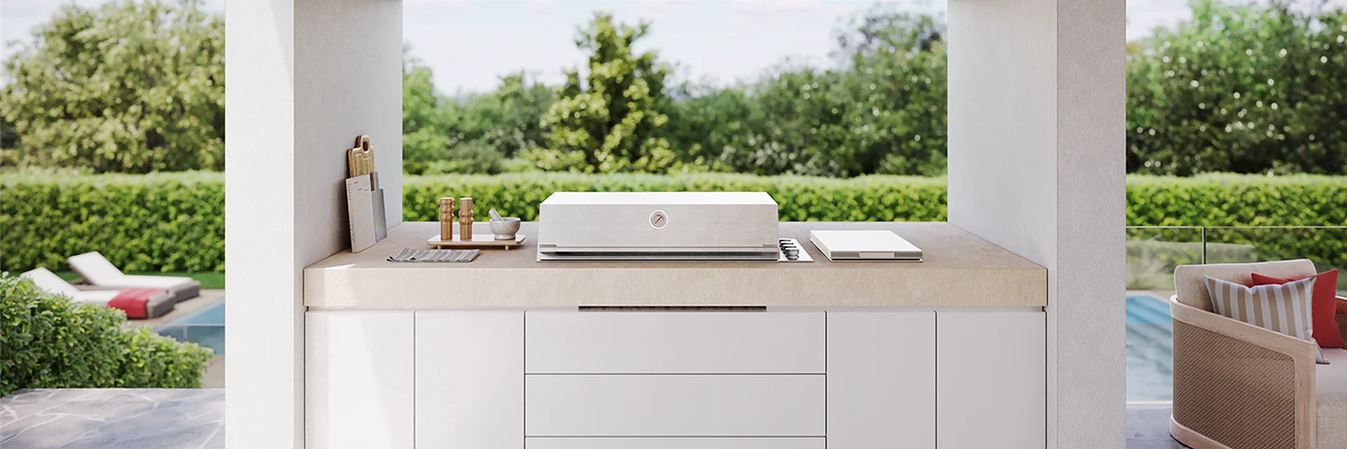 BeefEater ProLine built-in barbecue in a white outdoor kitchen under a timber-lined pergola with a rangehood above, opening onto a garden and pool