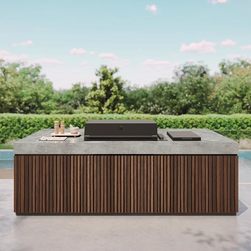 BeefEater ProLine built-in barbecue with a dark hood set into an outdoor kitchen island with a concrete worktop and timber slats, beside a pool and a hedge