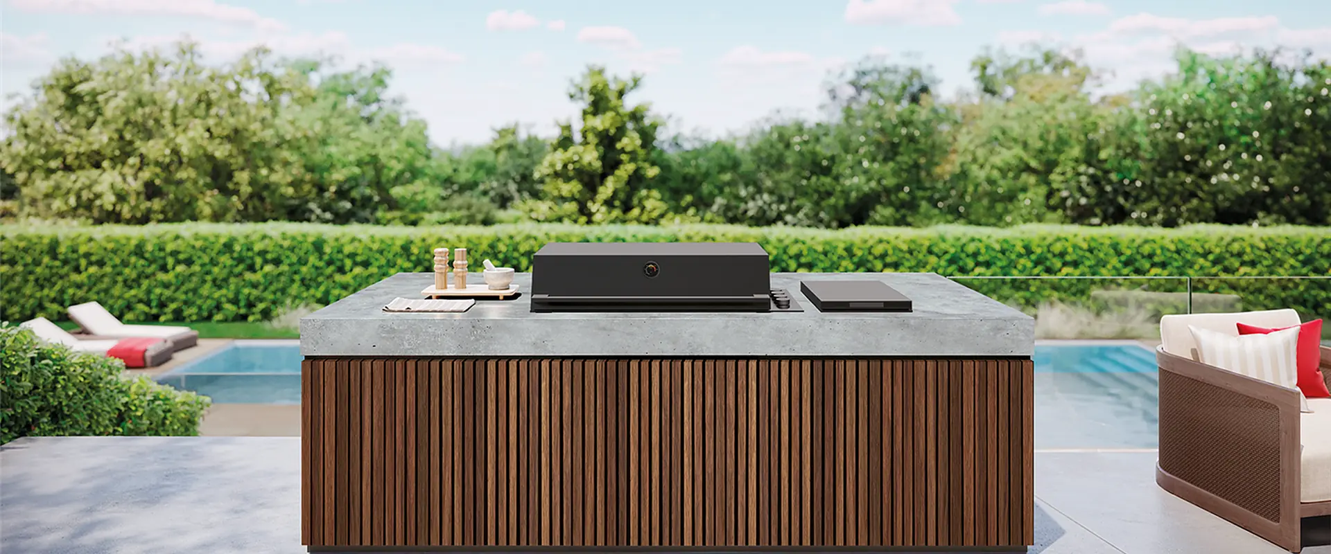 BeefEater ProLine built-in barbecue in the dark Monument finish set into a timber-clad island with a concrete worktop, on a terrace beside a pool