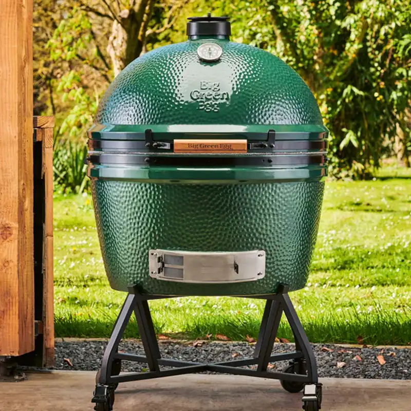 Big Green Egg 2XL kamado filling the frame on a rolling stand on a concrete terrace, with a sunny lawn behind