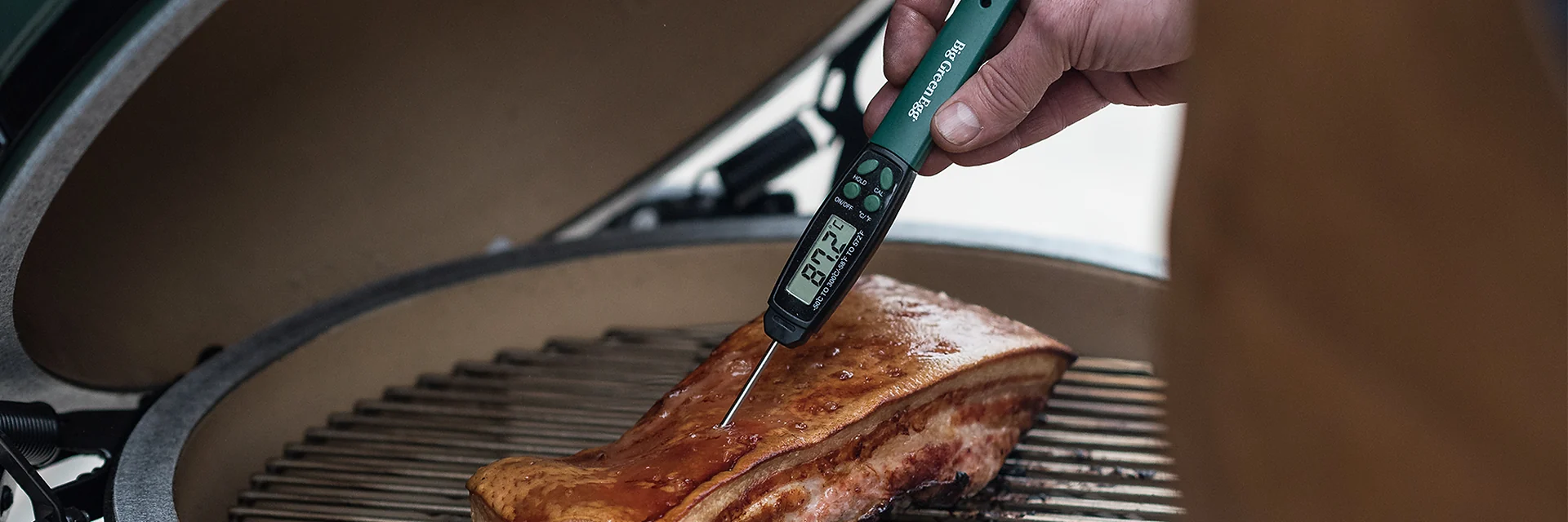 Digital probe thermometer held in a piece of meat on the cooking grid of a Big Green Egg kamado