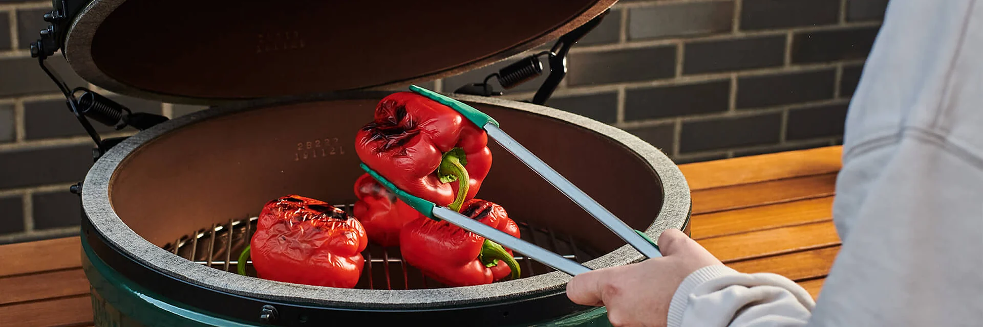 Red peppers on the grid of an open Big Green Egg kamado, turned with tongs