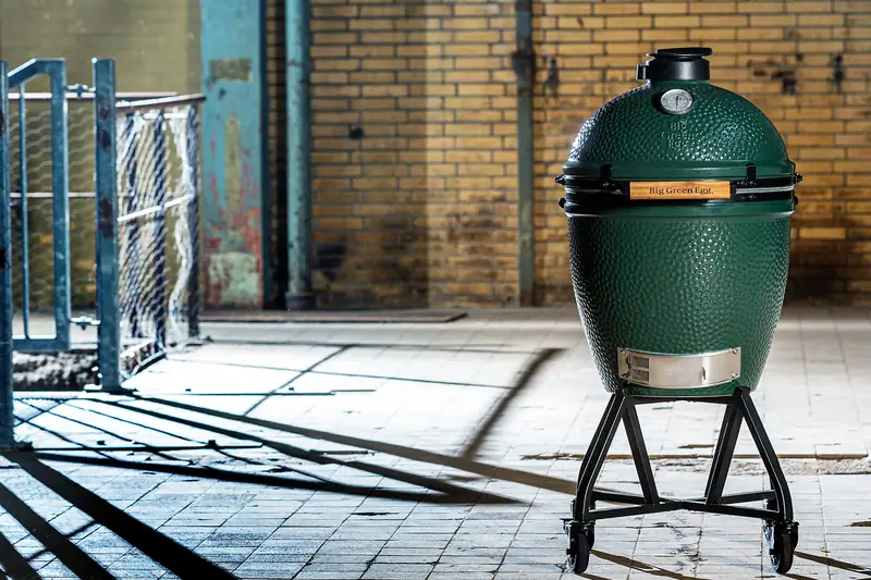 Big Green Egg kamado on its nest stand in a sunlit courtyard with a brick wall