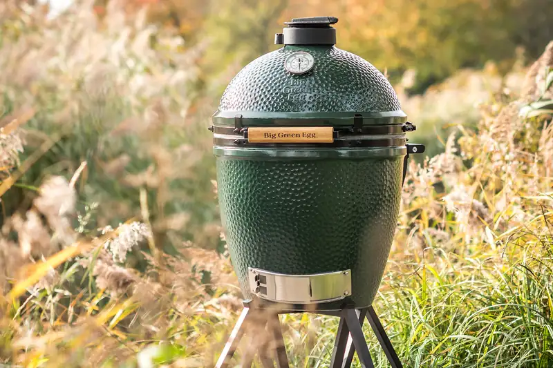 Big Green Egg kamado on its nest stand among tall grasses and wild flowers in warm evening light