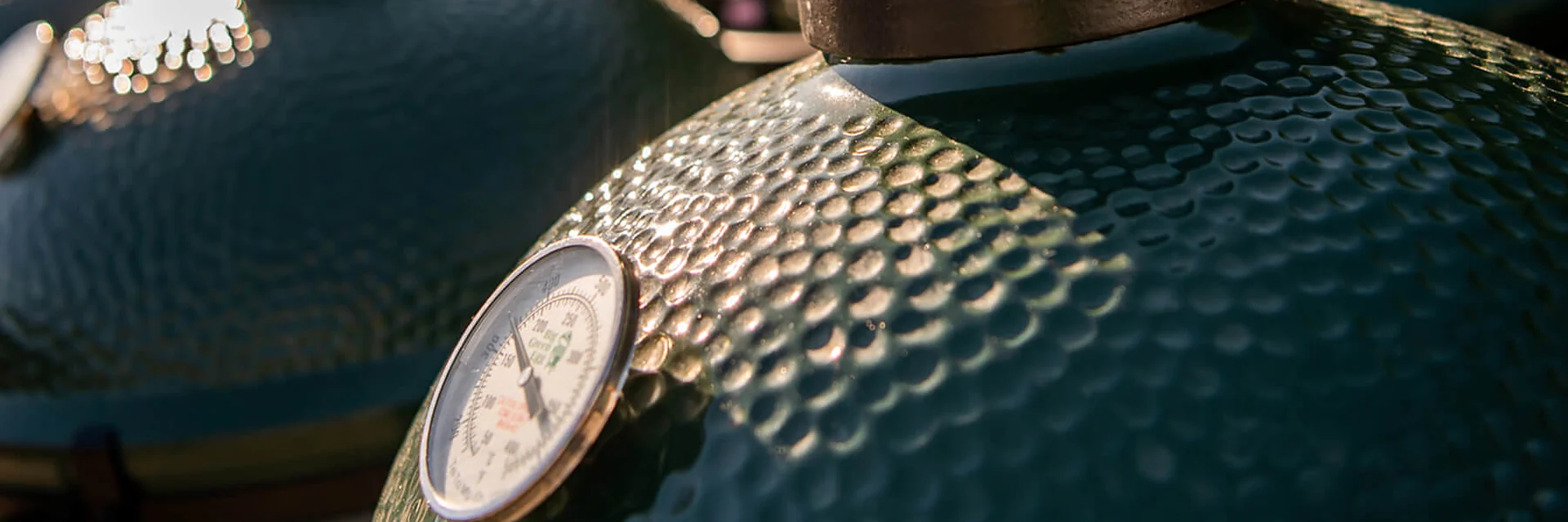 Row of Big Green Egg kamados seen close up, with the temperature gauge and vent cap of the nearest one in focus