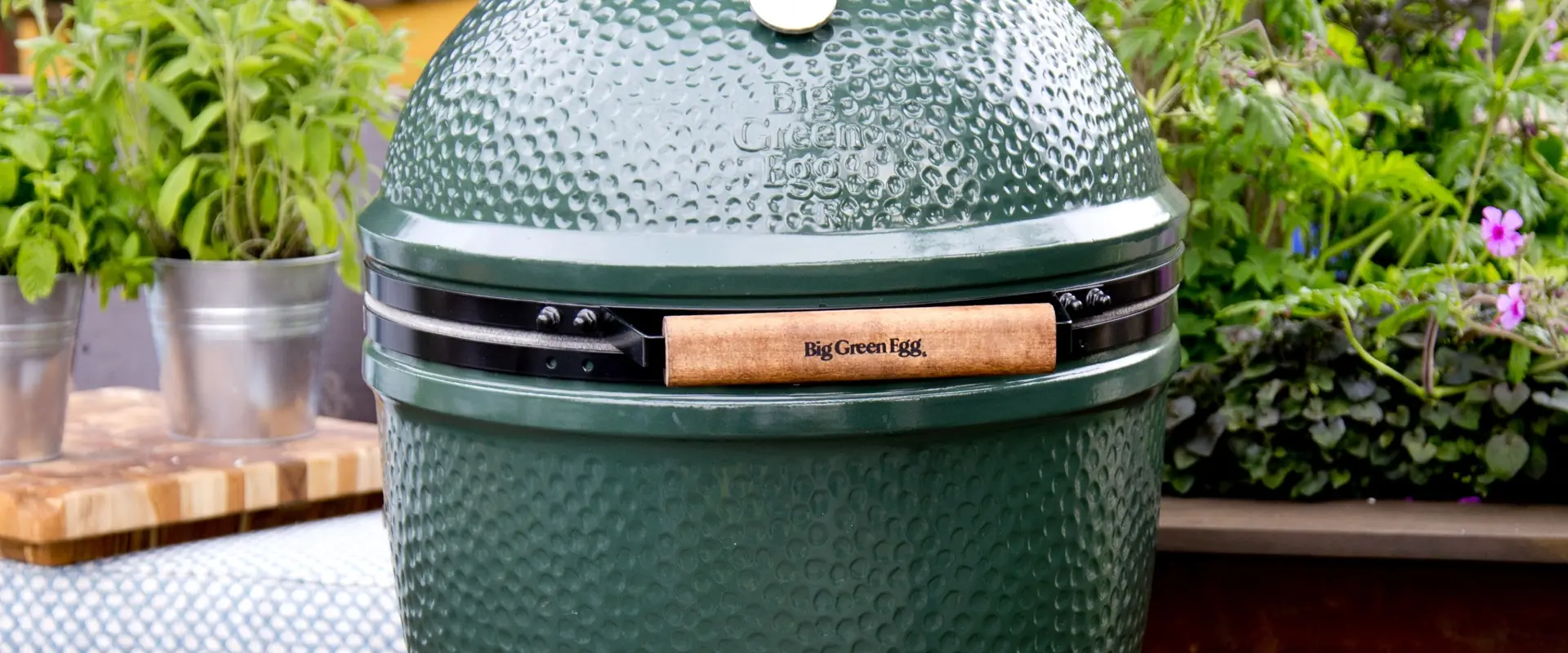 Big Green Egg Large ceramic kamado with its dimpled green glaze and wooden handle, among potted herbs on a garden deck