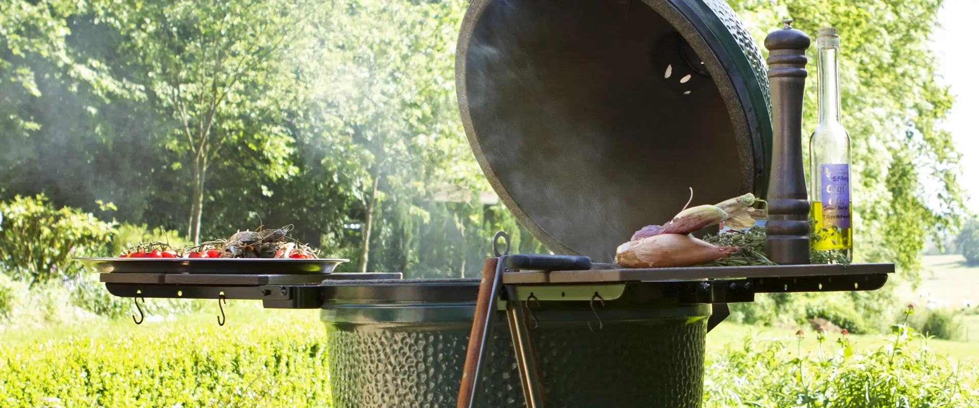 Big Green Egg Large kamado with its lid open and smoke rising in a garden