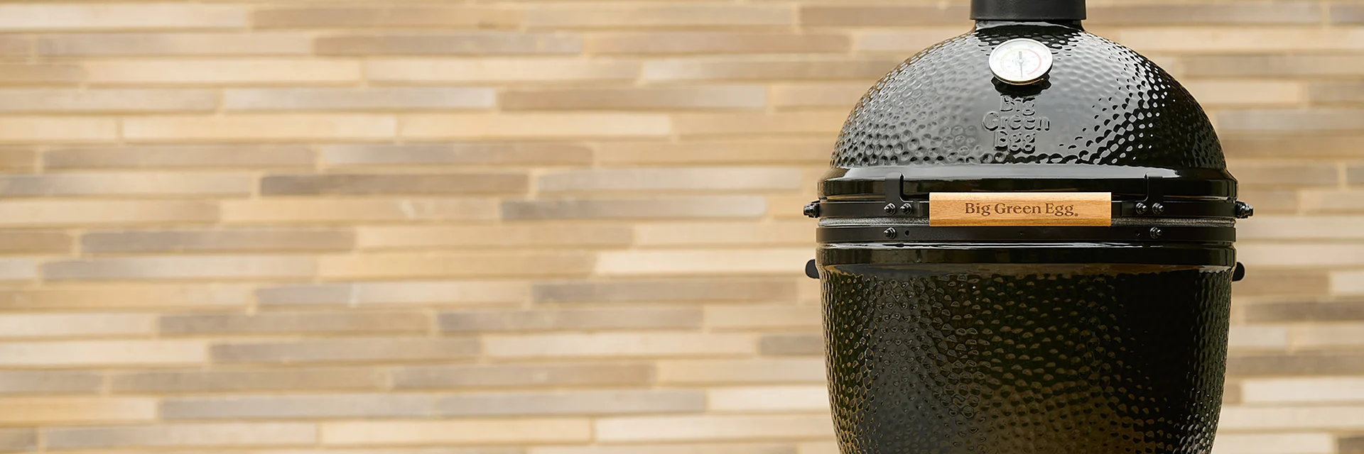 Black Big Green Egg Large from The Onyx edition on its nest in front of a sunlit stone-brick wall