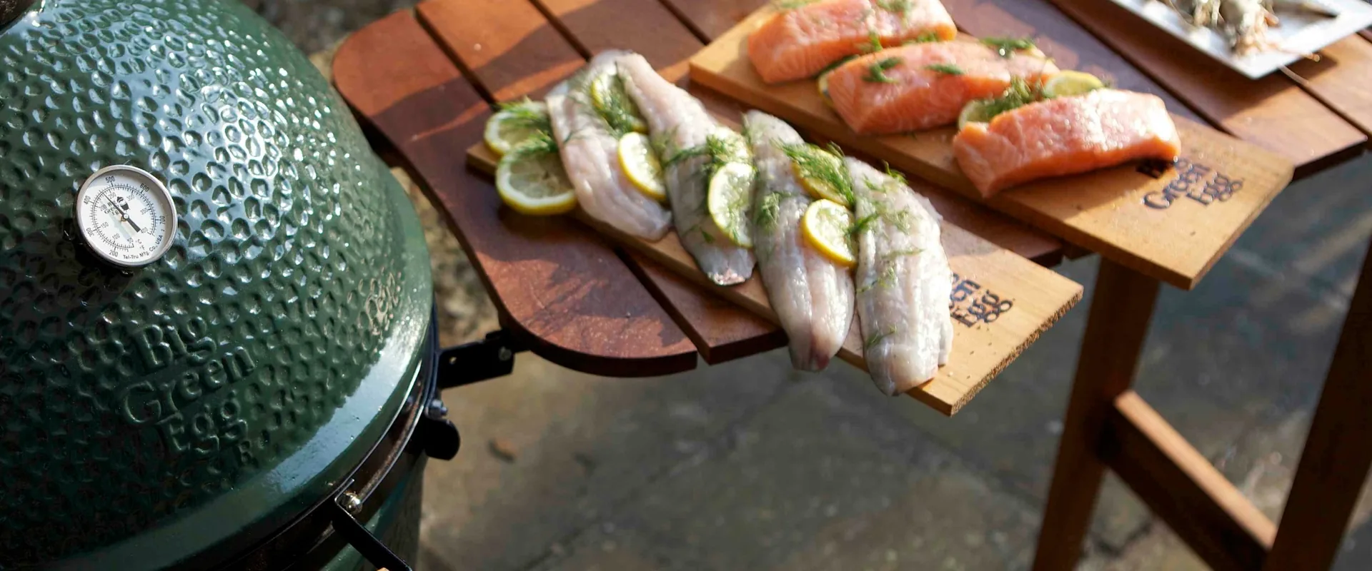 Big Green Egg Medium kamado cooking fish on cedar planks, set on an outdoor table