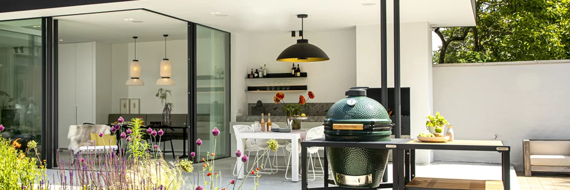 Big Green Egg kamado in a black modular table with wooden shelves on the terrace of a modern white villa with a garden