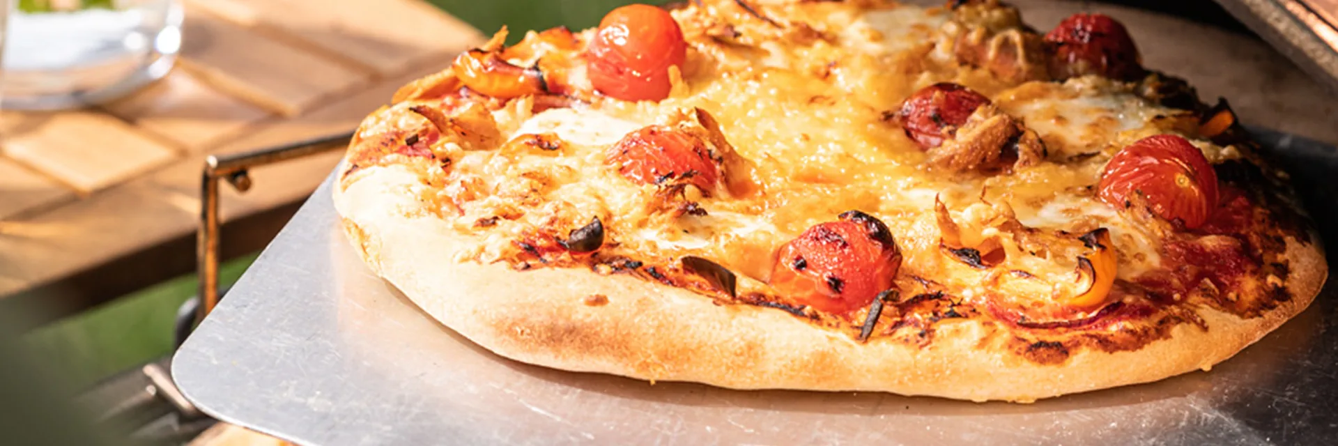 Freshly baked pizza being lifted on a metal peel from a Big Green Egg kamado