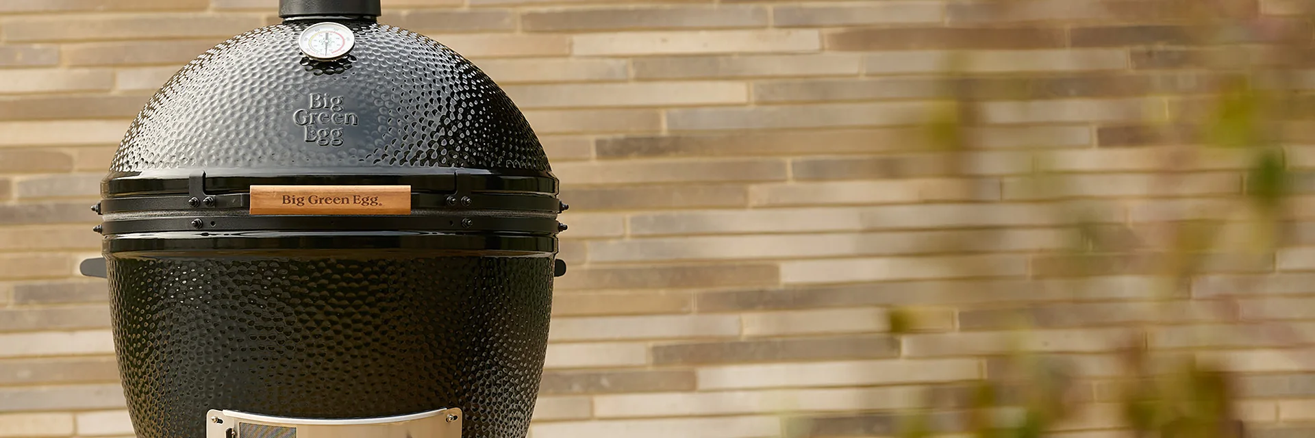 Black Big Green Egg XLarge from The Onyx edition on its rolling nest by a stone-brick wall
