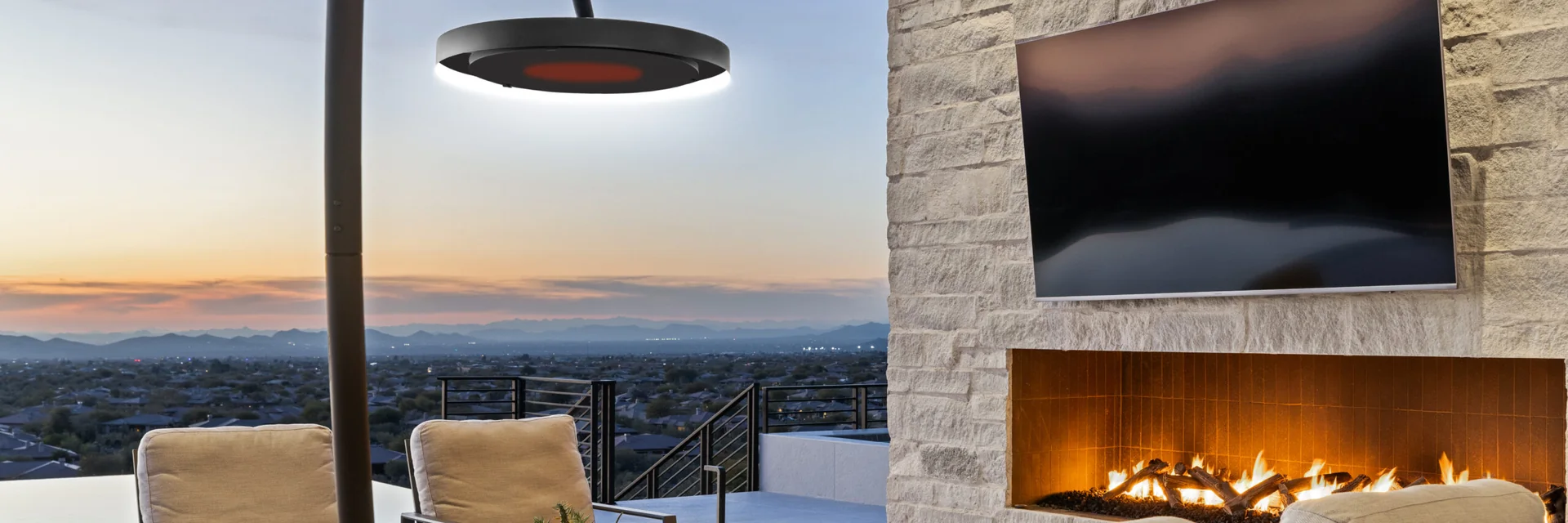 Bromic Eclipse heater over armchairs on a terrace at sunset, beside a stone wall with a fireplace