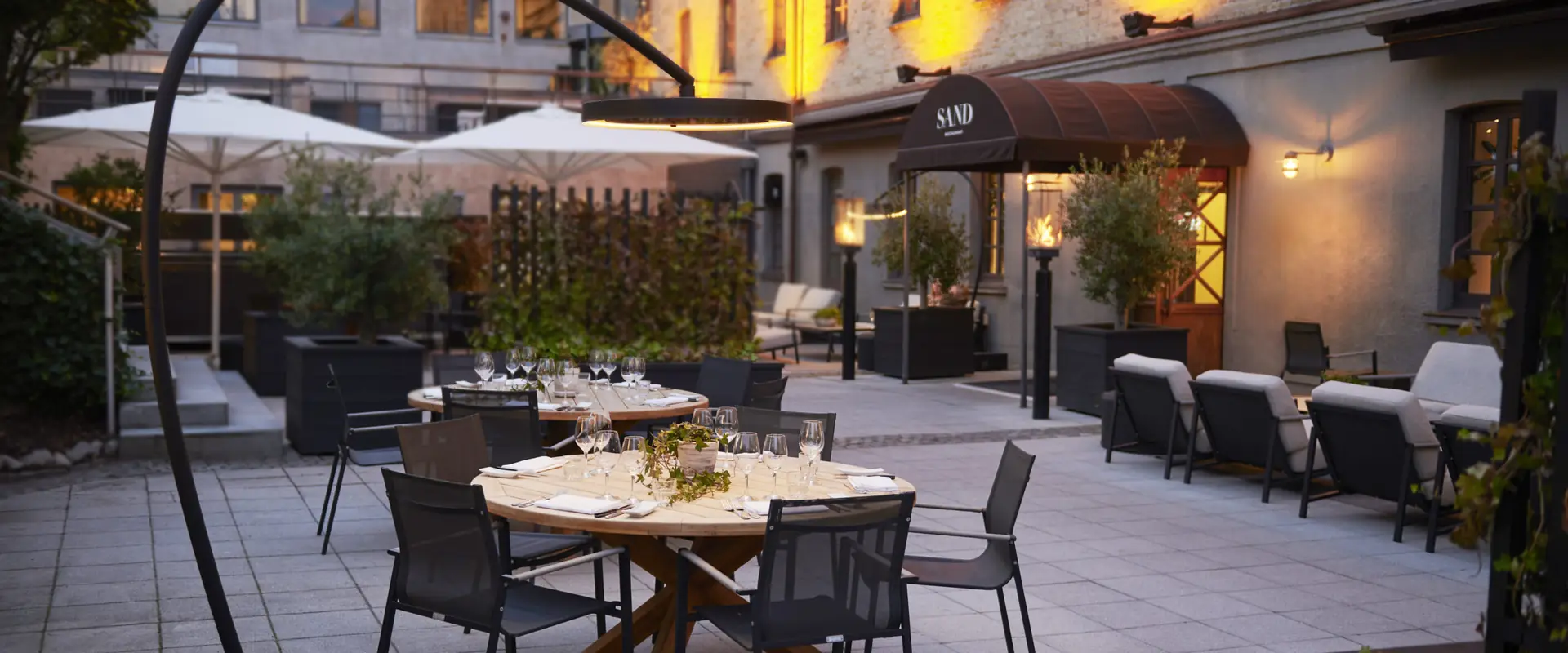 Bromic Eclipse Portable electric heater arching over a set dining table in a hotel restaurant courtyard at dusk