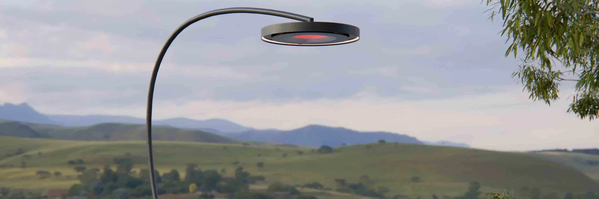 Bromic Eclipse Portable heater with its curved arm and glowing ring above an outdoor sofa, overlooking a valley at dusk