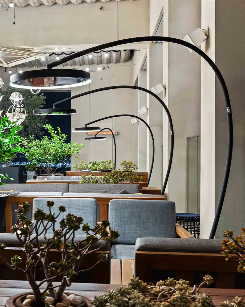 Bromic Eclipse Portable heaters with curved black arms and glowing light rings arching over lounge seating and potted trees on a bar terrace