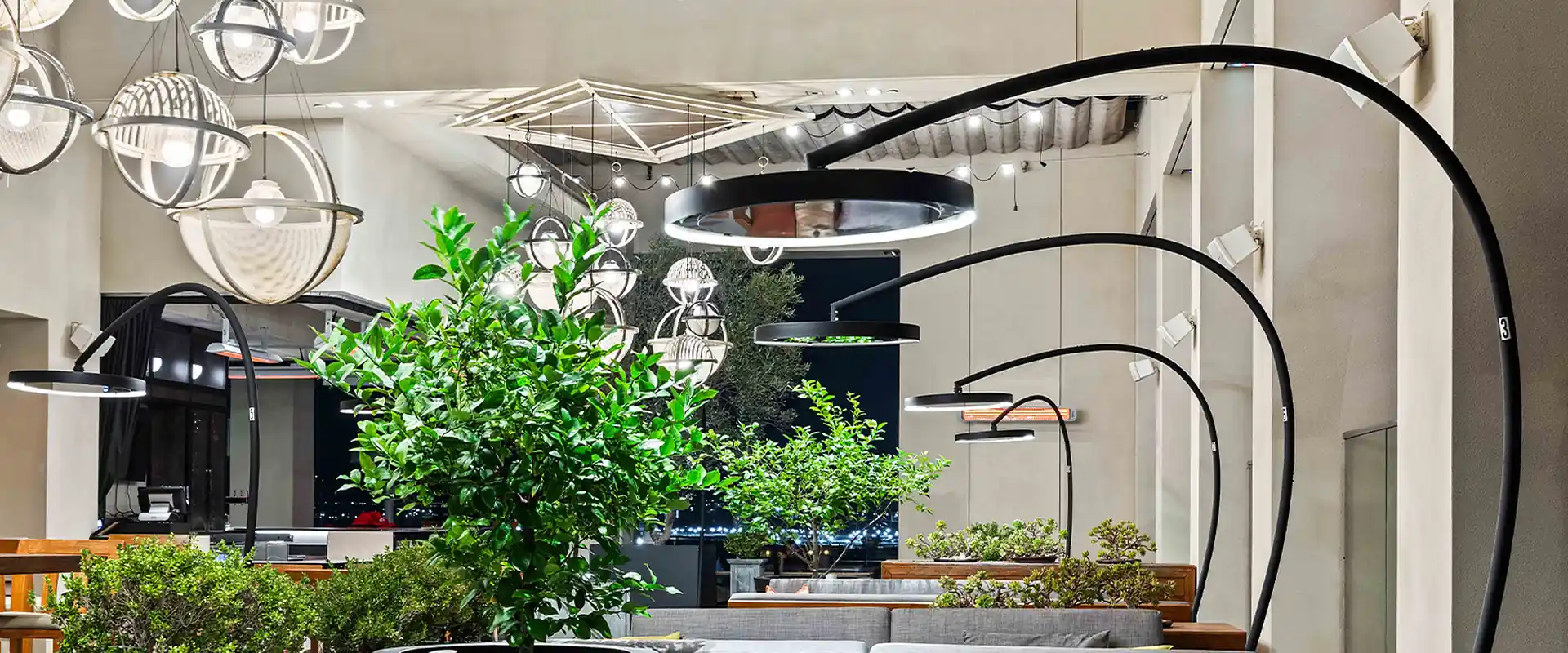 Bromic Eclipse Portable heaters with curved black arms and glowing light rings arching over lounge seating and potted trees on a bar terrace