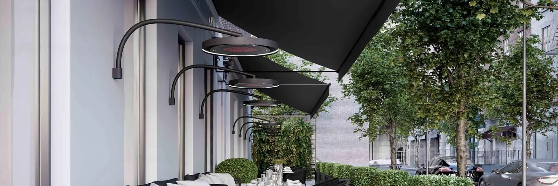 Row of Bromic Eclipse wall-mounted electric heaters above a pavement restaurant terrace with a black awning and boxwood planters