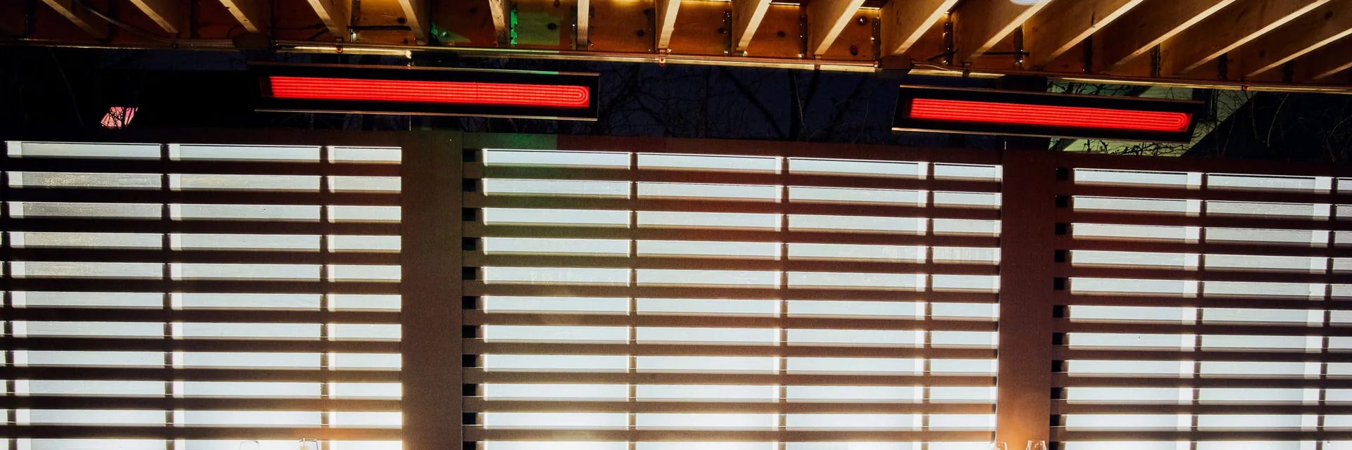 Bromic electric heaters glowing under a slatted ceiling above the tables of a restaurant