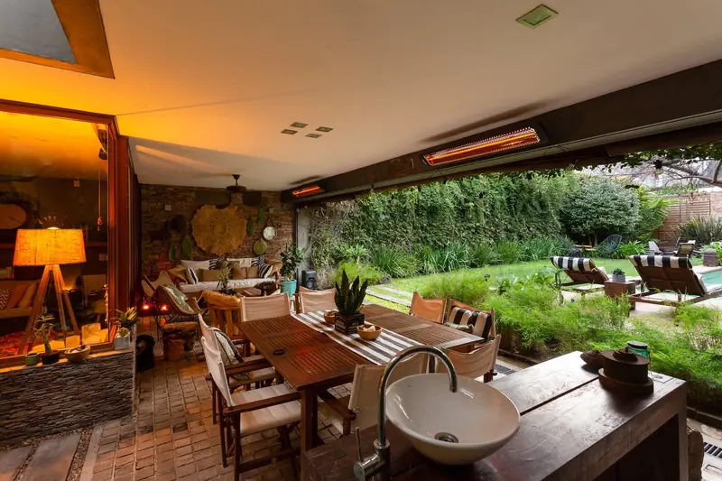 Bromic heaters under the roof of a covered terrace with a long dining table, open to a garden