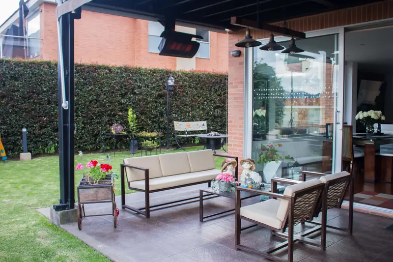 Bromic heaters under the roof of a covered garden terrace with a sofa and armchairs