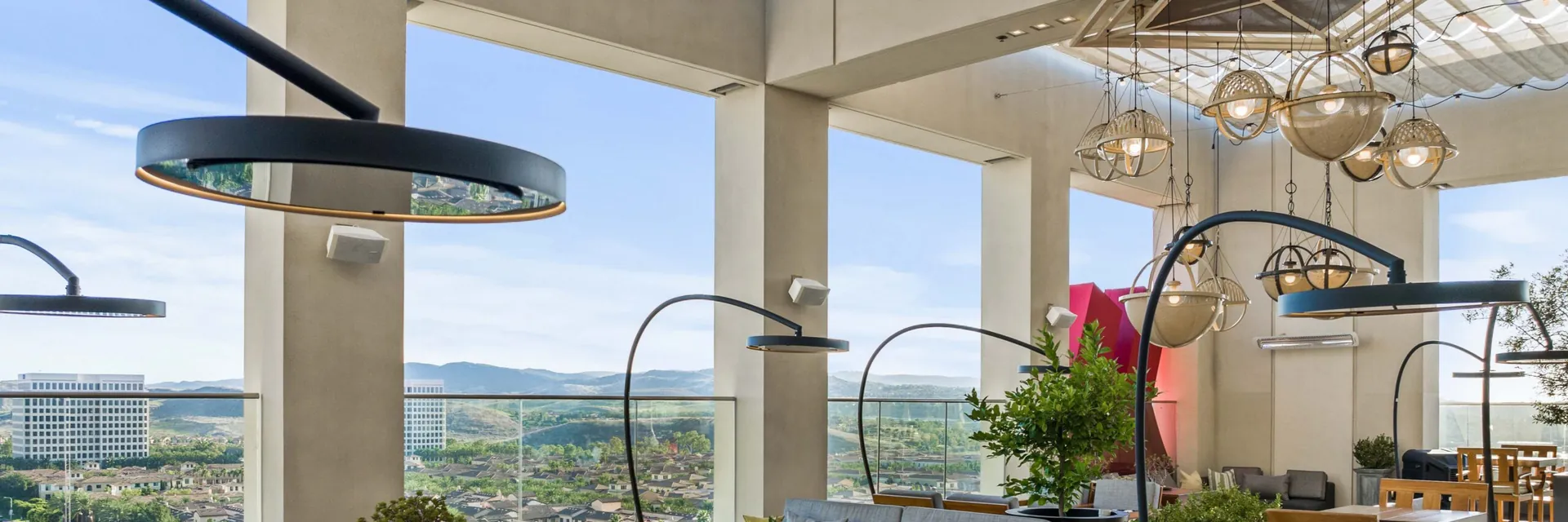 Bromic heaters on curved poles over the tables and planters of a rooftop terrace by day, with hills in the distance