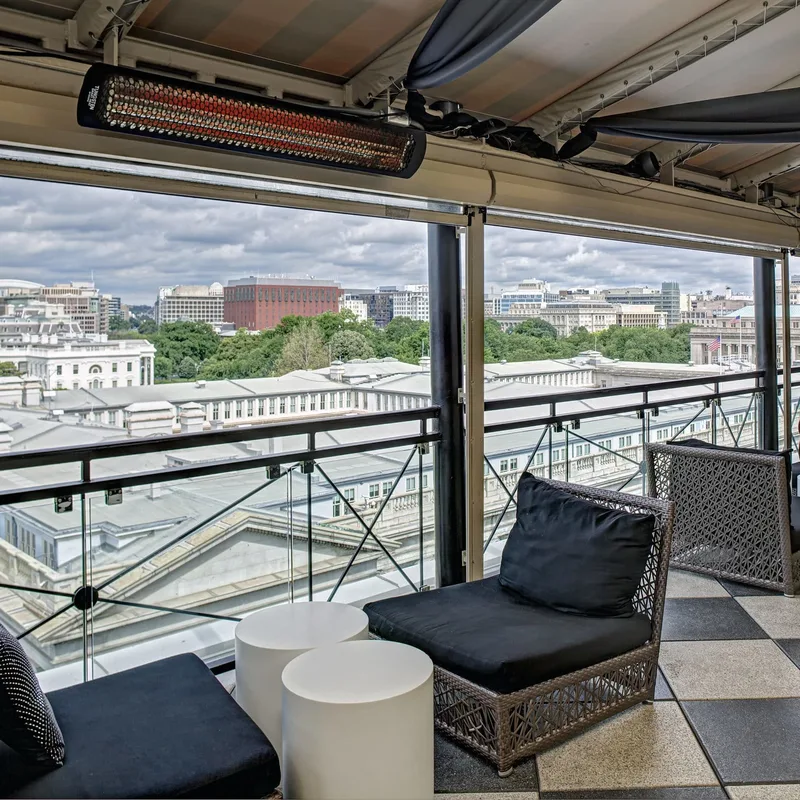 Bromic heater under the canopy of a hotel rooftop lounge with dark armchairs and a view over the city