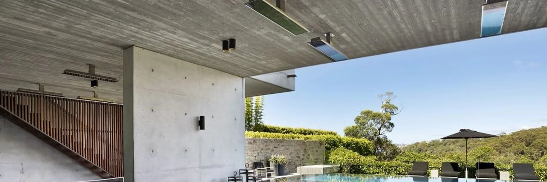 Bromic Platinum Smart-Heat Electric heaters set into the board-marked concrete ceiling of a covered terrace, with a lawn and an infinity pool beyond