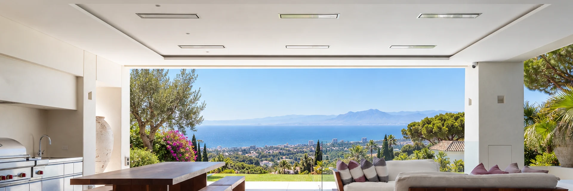 Bromic Platinum Electric heaters recessed in the ceiling of a covered terrace with an outdoor kitchen, dining table and sofas, overlooking the Mediterranean
