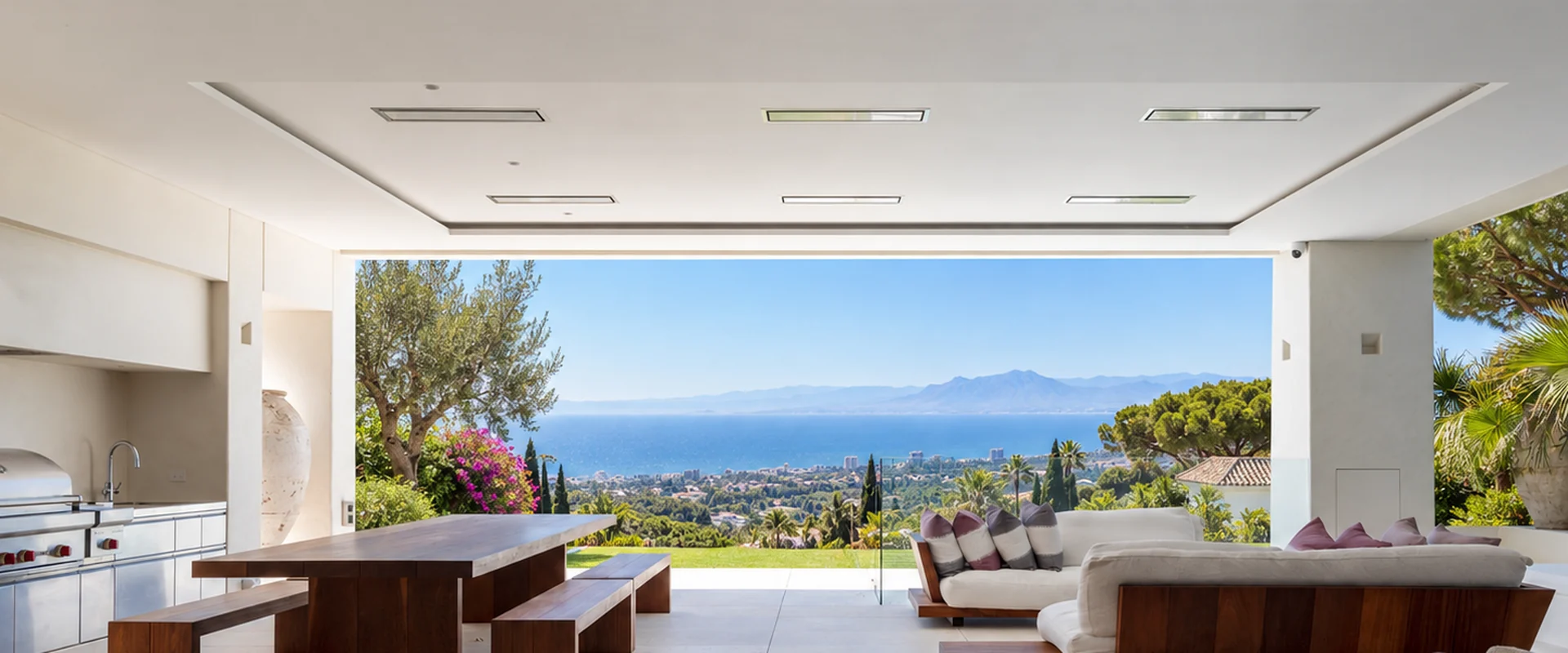 Bromic Platinum Electric heaters recessed in the ceiling of a covered terrace with an outdoor kitchen, dining table and sofas, overlooking the Mediterranean