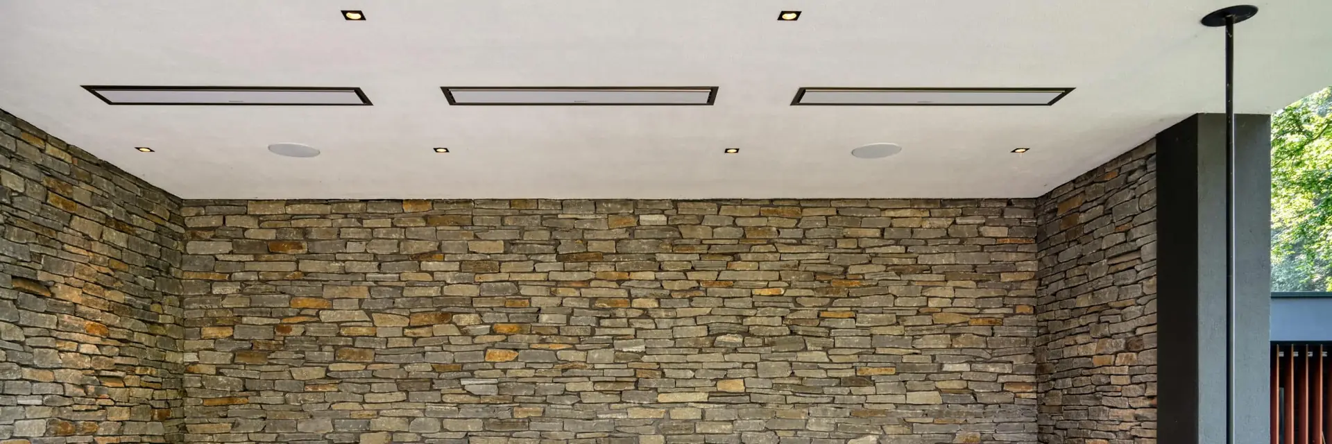 Three white Bromic Platinum Electric heaters flush-mounted in the white ceiling of a covered terrace with a dry-stone wall