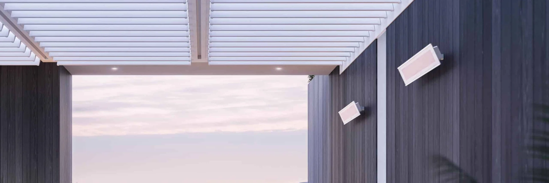 Two white Bromic Platinum Electric heaters mounted on a dark timber wall beneath a white louvered pergola, with hills at dusk beyond