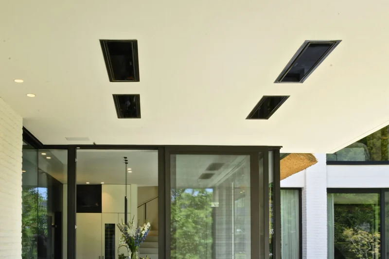 Four black Bromic Platinum Smart-Heat Electric heaters recessed in the white ceiling of a covered terrace, above black-framed glass doors