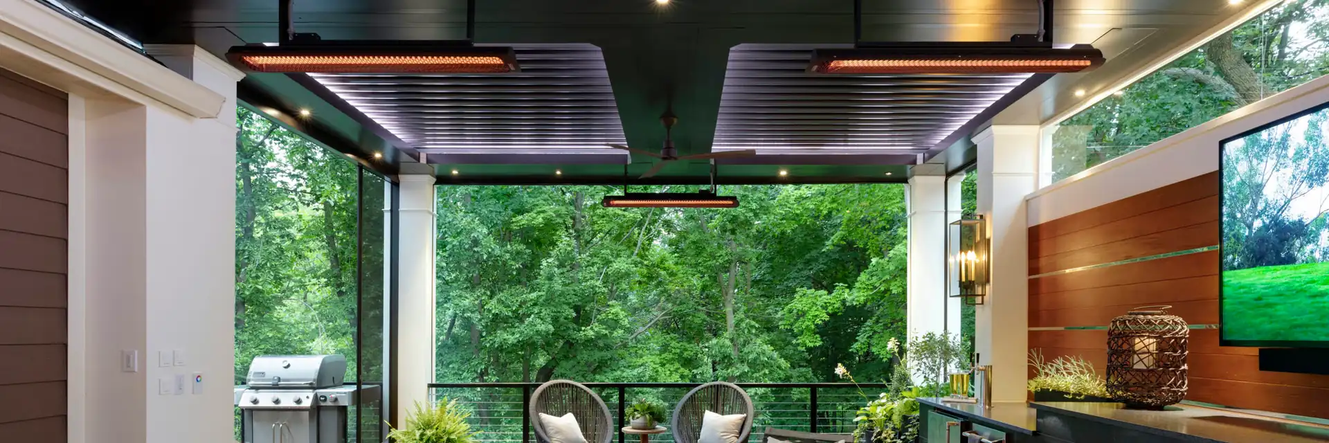 Black Bromic Tungsten Electric heaters under the dark ceiling of a covered deck with a white sofa, a linear fireplace and trees all around