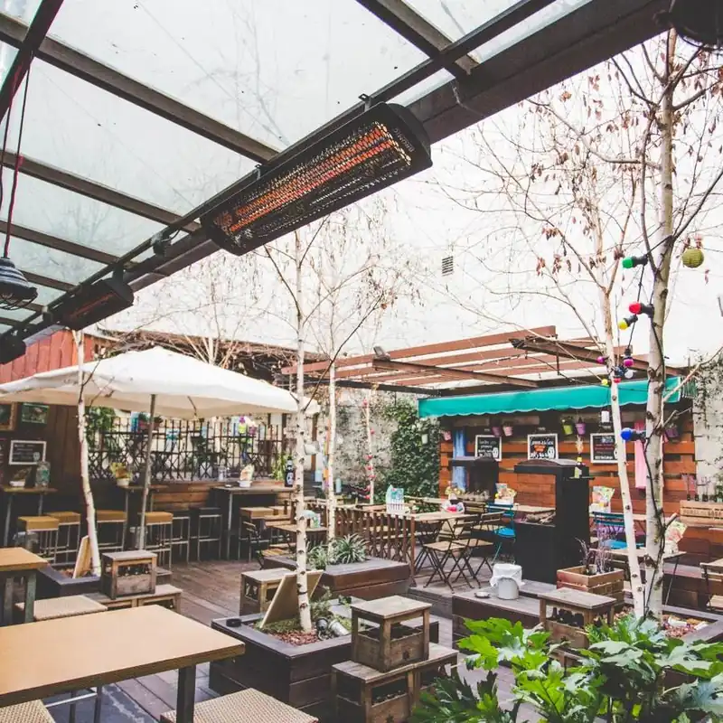 Black Bromic Tungsten Electric heater glowing under the glass roof of a restaurant patio with birch trees, wooden tables and white parasols