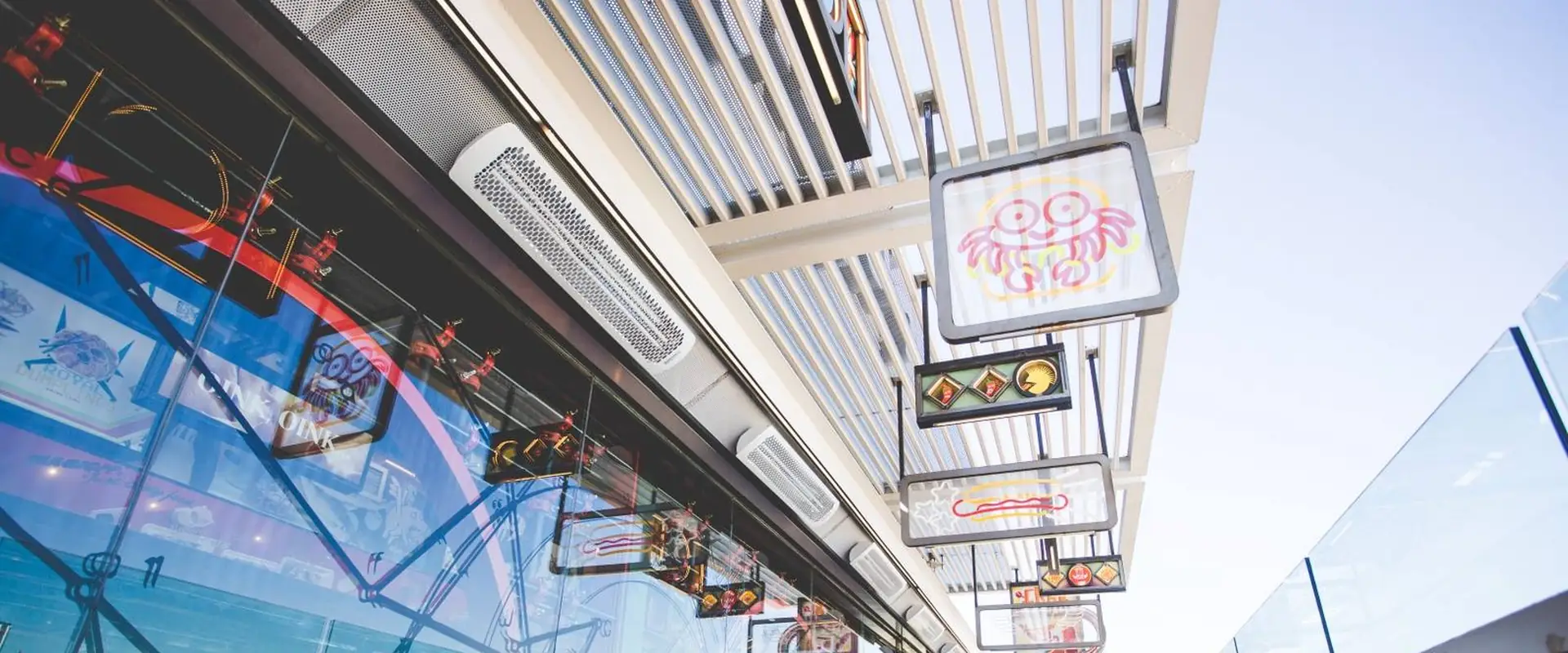 White Bromic Tungsten Electric heaters fixed along the glazed front of a rooftop restaurant terrace in Madrid, with neon signs hanging from the pergola