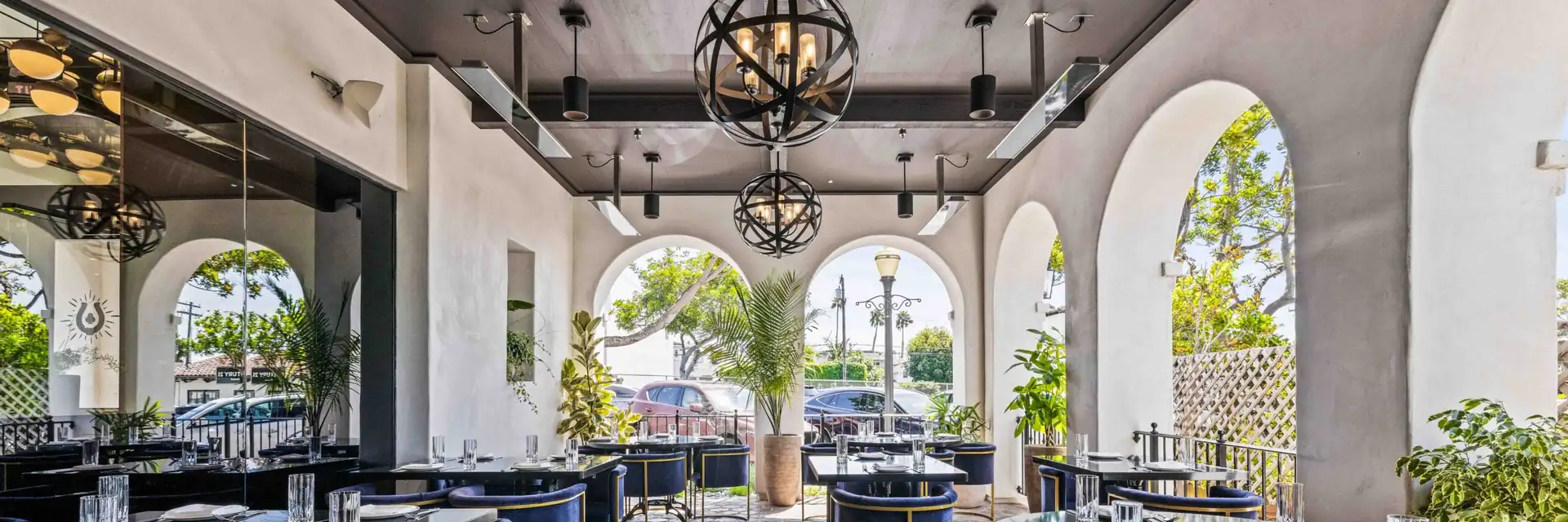 White Bromic Tungsten Electric heaters on the dark ceiling of a restaurant terrace with white arches, iron chandeliers and blue velvet chairs