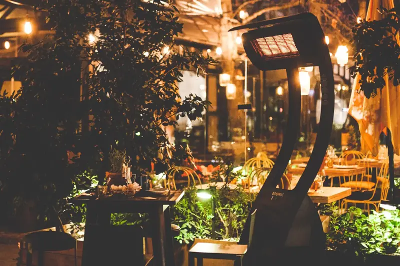 Bromic Tungsten Portable gas heater glowing at night on a restaurant terrace with string lights, set tables and greenery