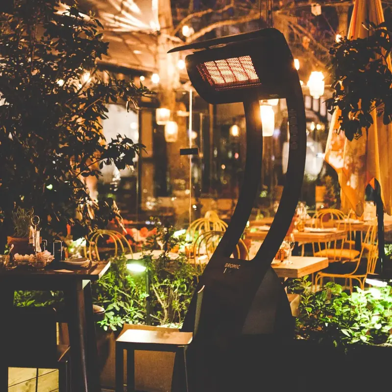 Bromic Tungsten Portable gas heater glowing at night on a restaurant terrace with string lights, set tables and greenery
