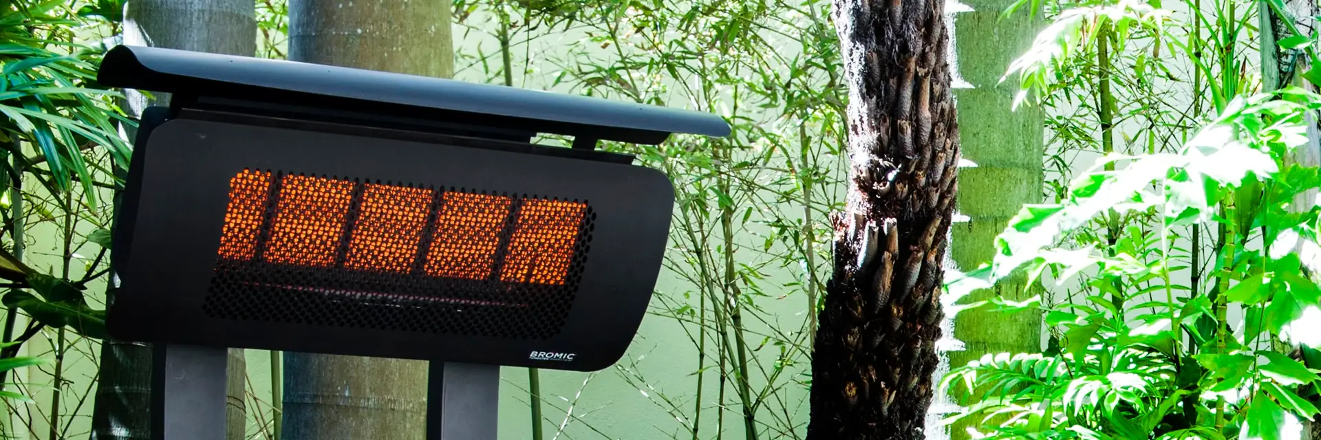 Close view of the glowing ceramic burners of a Bromic Tungsten Portable gas heater, with bamboo and lush foliage behind