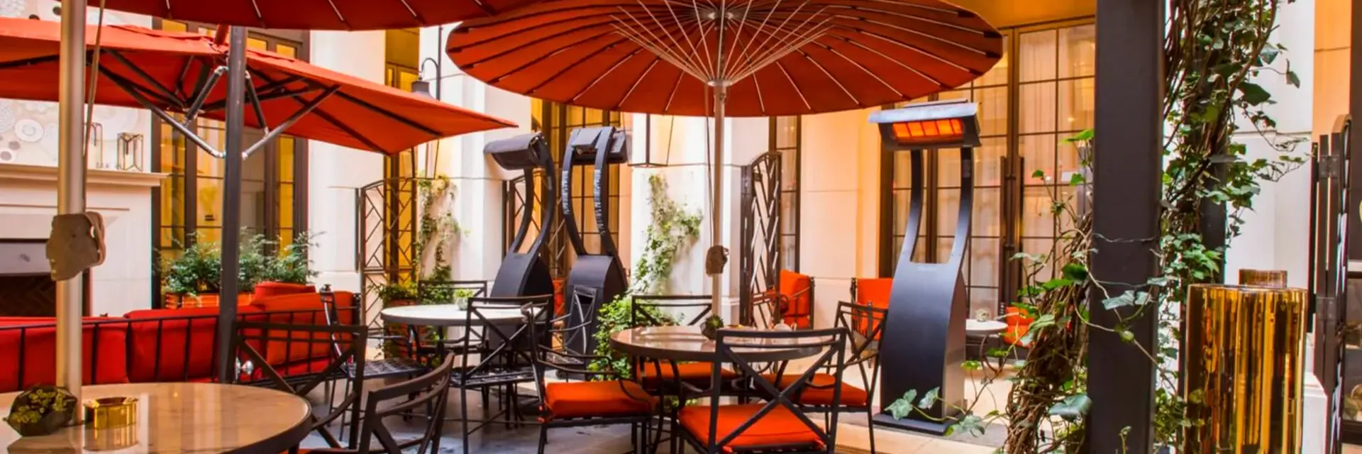 Three Bromic Tungsten Portable gas heaters among red parasols and orange-cushioned chairs on an elegant restaurant courtyard terrace