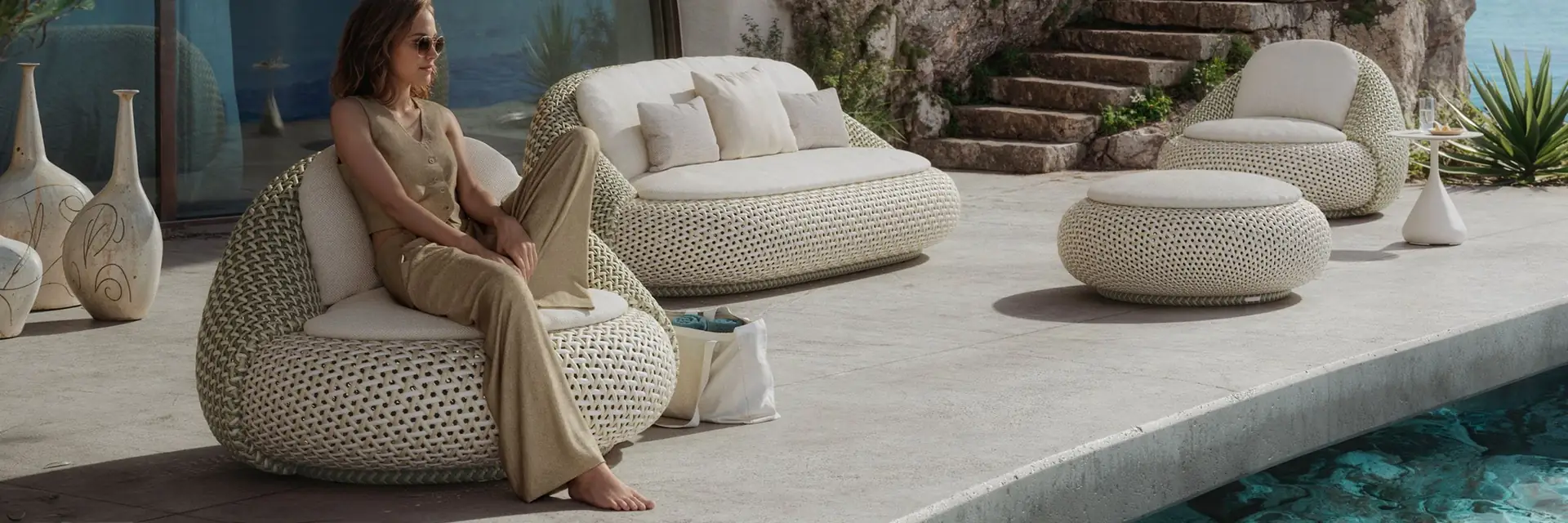 Woman relaxing in a Dedon Atolo armchair beside an Atolo sofa and footstools on a curved pool terrace cut into a cliff