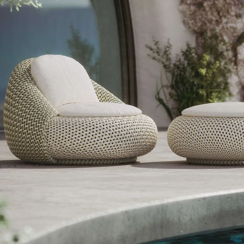 Dedon Atolo woven lounge chair with a white cushion and matching footstool on a stone terrace beside a pool