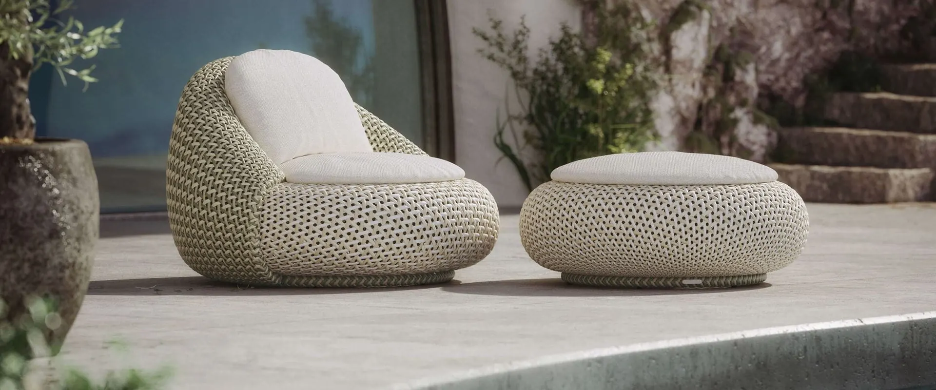 Dedon Atolo woven lounge chair with a white cushion and matching footstool on a stone terrace beside a pool
