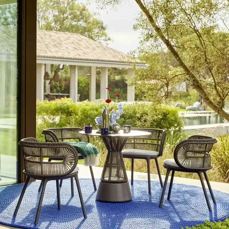 Dedon Cirql Nu woven armchairs around a round bistro table on a blue rug, looking onto a sunny garden