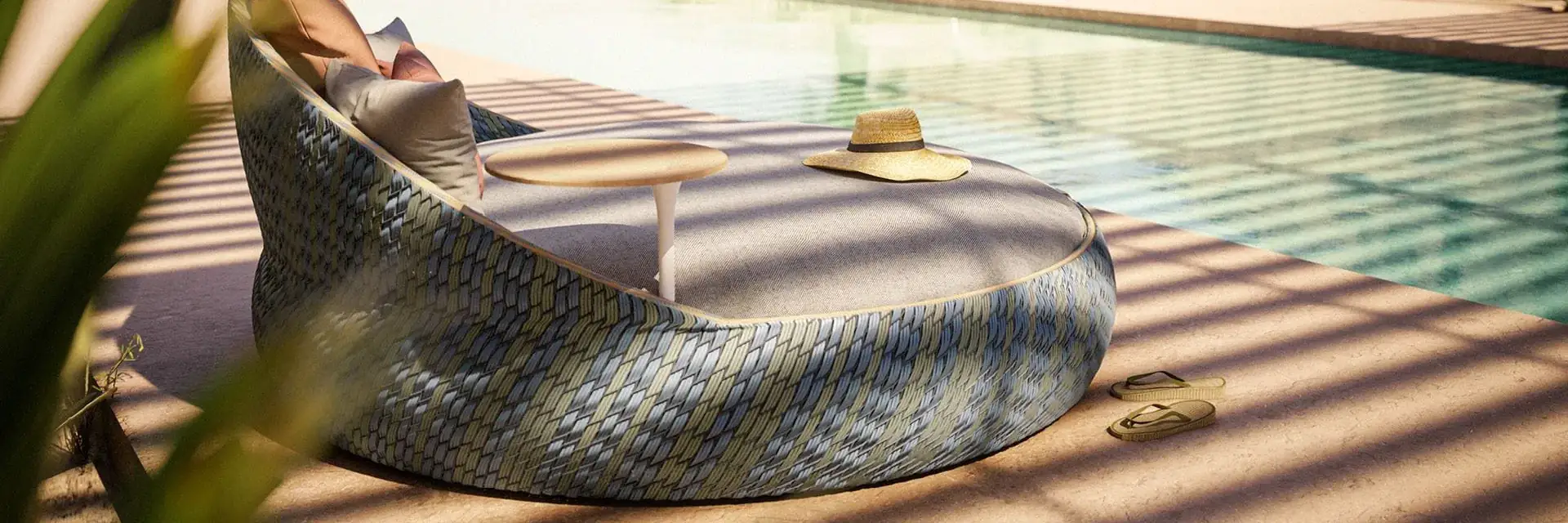 Dedon Dala round woven daybed with cushions beside a pool, with palm trees and desert hills behind